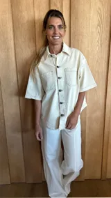 Sobrecamisa color beige de denim suave, con cuello clásico, manga corta, cierre frontal con botones y dos bolsillos de parche en el pecho.