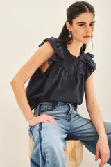 Camisa azul marino sin mangas con escote redondo y detalles de puntilla en canesú y volados con terminación de puntilla en mangas.