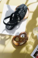 Sandalias negras con tiras anchas de cuero trenzado, hebilla dorada y tira trasera ajustable.