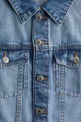 Vestido midi de denim celeste, con cuello camisero, manga corta y botonadura frontal. Presenta bolsillos superiores con solapa y botón, canesú delantero y trasero, falda acampanada y costuras decorativas.