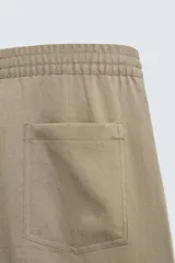 Pantalón negro de corte relajado con cintura elástica ajustable y pliegues en la parte delantera. Presenta bolsillos laterales y bolsillos traseros de parche.