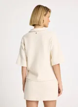 Chomba color crudo de tejido acanalado, corte holgado, cuello camisero, mangas cortas y anchas, bajo recto y caída estructurada.