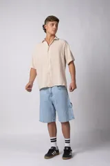 Camisa de hombre de manga corta color beige claro, confeccionada en lino. Tiene cuello clásico, cierre frontal con botones y corte recto.