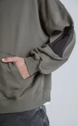 Canguro verde militar de algodón rústico, corte oversize, con capucha forrada, bolsillo tipo canguro y bolsillo en la manga con cierre.