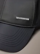 Gorra de béisbol negra con acabado satinado y visera curva. Presenta una placa metálica rectangular con el logo de Calvin Klein grabado en la parte frontal.