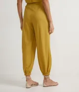 Pantalón harem color mostaza, con cintura elástica ancha, pliegues delanteros y horizontales, barra ajustada con elástico y pliegues.
