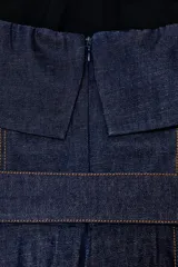 Mono largo de denim azul oscuro, estilo strapless con escote recto y detalle de volado en el busto. Incluye un cinturón del mismo tejido con hebilla forrada. El pantalón es de pierna ancha y presenta costuras verticales marcadas en contraste.