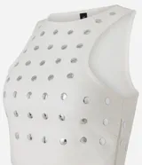 Top cropped sin mangas, color blanco, con escote redondo y tachuelas metalizadas distribuidas por toda la prenda. Posee cierre lateral de cremallera.