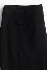 Pantalón negro de corte sastrero con cintura estándar, cierre y botón. Tiene bolsillos al bies en la parte delantera y bolsillos insertados decorativos en la parte trasera. Las piernas son acampanadas.