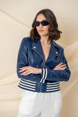 Chaqueta azul de cuero ecológico con cierre frontal asimétrico y cuello con solapas. Tiene puños elásticos a rayas blancas y azules, cierres metálicos plateados y un bolsillo en la manga.