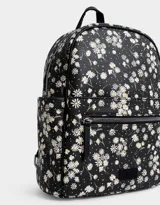 Mochila negra con estampado de margaritas blancas, confeccionada en cuero sintético. Cuenta con correas regulables, manija superior, acceso con cierre, bolsillo frontal con cierre y tag de cuerina. Incluye un pouch extraíble.