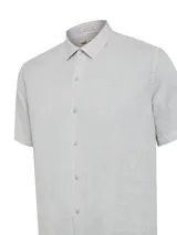 Camisa de manga corta para hombre, confeccionada en lino 100% orgánico color plateado. Tiene cuello clásico, cierre frontal con botones y un pequeño bolsillo en el pecho.