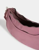 Bandolera hobo negra de tela deportiva con correa regulable, cierre superior, bolsillo frontal y charm lateral decorativo.