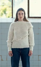 Sweater tejido a crochet en lana merino color crudo, con cuello redondo y manga larga. Presenta una trenza diagonal con volados en el frente.