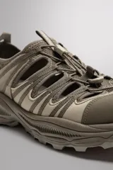 Zapatilla deportiva color beige con aberturas laterales, ajuste de cordones y suela de goma.