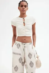 Pantalón de corte holgado en tejido liviano de mezcla de lino y viscosa, color crudo con estampado paisley en marrón. Modelo con cintura elástica fruncida y cordón para ajustar, bolsillos laterales discretos y piernas rectas con bajo deshilachado.