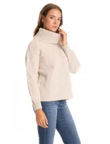 Buzo de punto grueso color beige, con cuello volcado y textura en relieve. Tiene mangas largas de corte hombro caído y puños anchos.