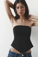 Top bustier negro sin mangas, con escote recto y bajo asimétrico. Cierre lateral con cremallera oculta.