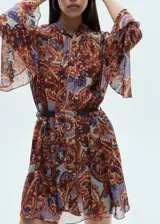 Vestido corto evasé con estampado paisley en tonos marrón, naranja y lila. Tiene cuello redondo con lazo, mangas largas con volantes, forro interior y cinturón desmontable.
