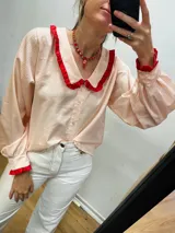 Camisa de algodón a rayas verticales color rosa y blanco, con cuello babero y puños con volantes rojos.