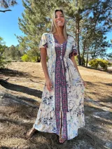 Vestido largo de seda con estampado floral en tonos celeste, rosa y beige, con mangas cortas y volantes en el ruedo.