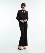 Blusa negra de chiffon con cuello alto con lazo, mangas largas con puños ajustados, detalle de volado delantero y volado en encaje.