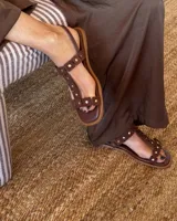 Sandalias chatas de cuero vacuno color marrón con tiras con apliques de tachas doradas.