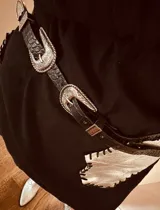 Cinturón de cuero negro con hebilla plateada y riñonera plateada con flecos.