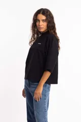 Remera blanca de corte cuadrado con cuello subido y mangas 3/4 amplias.