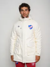 Parka blanca con capucha, cierre frontal con cremallera y botones a presión, cuatro bolsillos frontales con solapa y puños ajustables. Incluye logo de Umbro y escudo del Club Nacional de Football en el pecho.