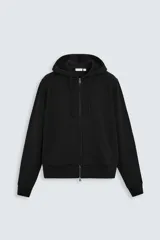 Sudadera negra relaxed fit confeccionada en tejido de algodón compacto con interior en rizo. Cuello con capucha ajustable y manga larga. Bolsillos frontales tipo canguro. Acabados en rib. Cierre frontal con cremallera.