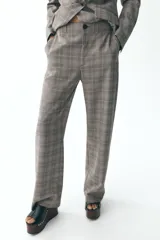 Pantalón de tiro alto con estampado de cuadros en tonos marrones y grises, con bolsillos delanteros y falsos bolsillos traseros. Cierre frontal con cremallera y botón.