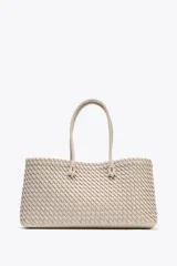 Bolso shopper alargado color beige con diseño trenzado, doble asa de hombro y cierre con botón imantado. Incluye bolsa interior con cierre fruncido.