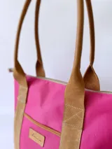 Bolso tipo tote de lona color fucsia con asas de cuero marrón, bolsillo interno y externo.