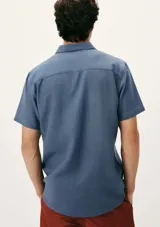 Camisa celeste de manga corta con cuello clásico, cierre frontal con botones y bolsillo de parche en el pecho. Corte recto.