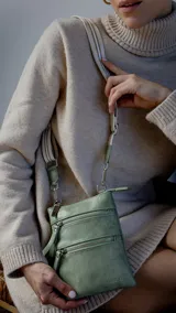 Bandolera tipo phone bag color verde militar, con correa larga regulable y desmontable. Tiene cierre metálico superior y dos bolsillos frontales con cierre.