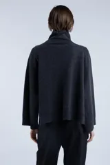 Sweater gris oscuro de lana con cuello alto y cierre asimétrico en el hombro. Presenta un calce levemente amplio y caída fluida, mangas largas con terminaciones acanaladas y aberturas laterales.