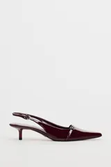 Zapato destalonado color borgoña charol, con tacón kitten y punta fina. Presenta una tira trasera con hebilla ajustable y detalle de hebilla metálica en la parte delantera.