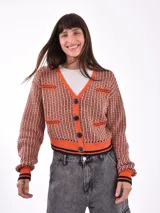 Cárdigan tejido con patrón geométrico en tonos naranja, negro y blanco. Tiene cuello en V, cierre con botones negros y ribetes a contraste en cuello, puños y bajo.