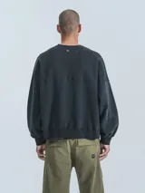 Buzo de cuello redondo, color negro, confeccionado en frisa gamuzada de algodón con recortes en microfibra, creando un efecto de capas. Presenta un bolsillo frontal tipo parche con cierre a presión.