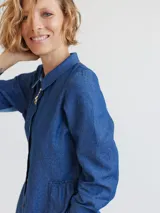 Camisa celeste de algodón con cuello clásico, cierre frontal con botones y mangas largas. Presenta volados en el frente y corte evasé.
