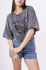 Remera gris oscuro con efecto lavado, corte crop y estampado frontal de mariposa con detalles tribales en negro.