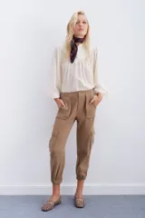 Pantalón de corderoy gris, de corte holgado, con elástico en la cintura, cierre y botón. Tiene bolsillos aplicados en el delantero y puños con elástico interno.