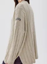 Buzo tejido color blanco, con cuello subido tipo polera, diseño oversized y largo con pequeños cortes laterales.