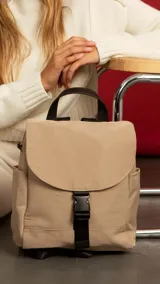 Mochila color beige de nylon con tapa y broche. Incluye bolsillos interiores, bolsillos laterales de fácil acceso, correas regulables y bolsillo en la espalda.