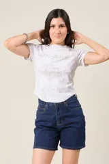 Remera blanca con estampado tie-dye en tonos grises y logo "LOU JEANS" con apliques brillantes.