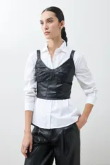 Top negro de eco cuero con corte crop, breteles finos y detalle de tul en el escote.