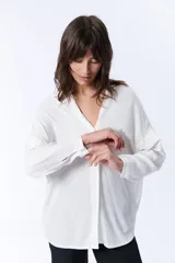 Blusa blanca de manga larga con escote en V y cierre frontal con botones.