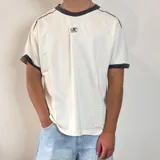 Remera de manga corta color crema con cuello redondo y ribetes en color gris oscuro. Presenta un pequeño logo bordado en el pecho con la palabra "SANTOS".