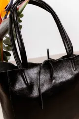 Bolso tote grande de cuero negro con doble asa larga y cierre superior con tira de cuero. Diseño minimalista y atemporal.